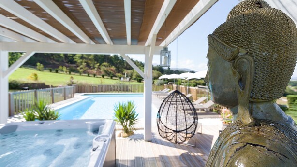 Ett bubbelbad, en Buddha-staty och en pool med utsikt över en vackert anlagd trädgård.