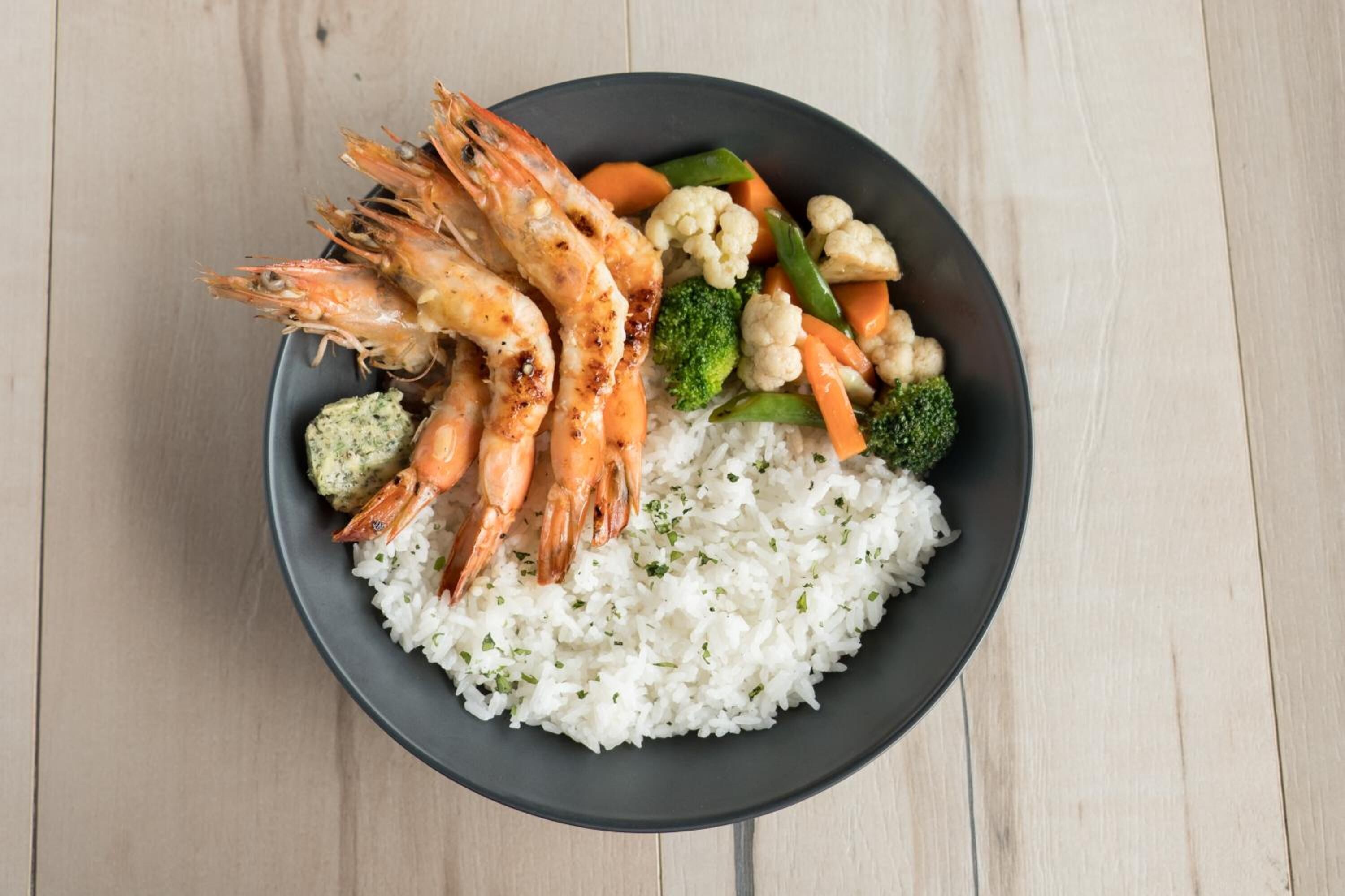 A bowl of rice with shrimp, broccoli, carrots, and cauliflower.
