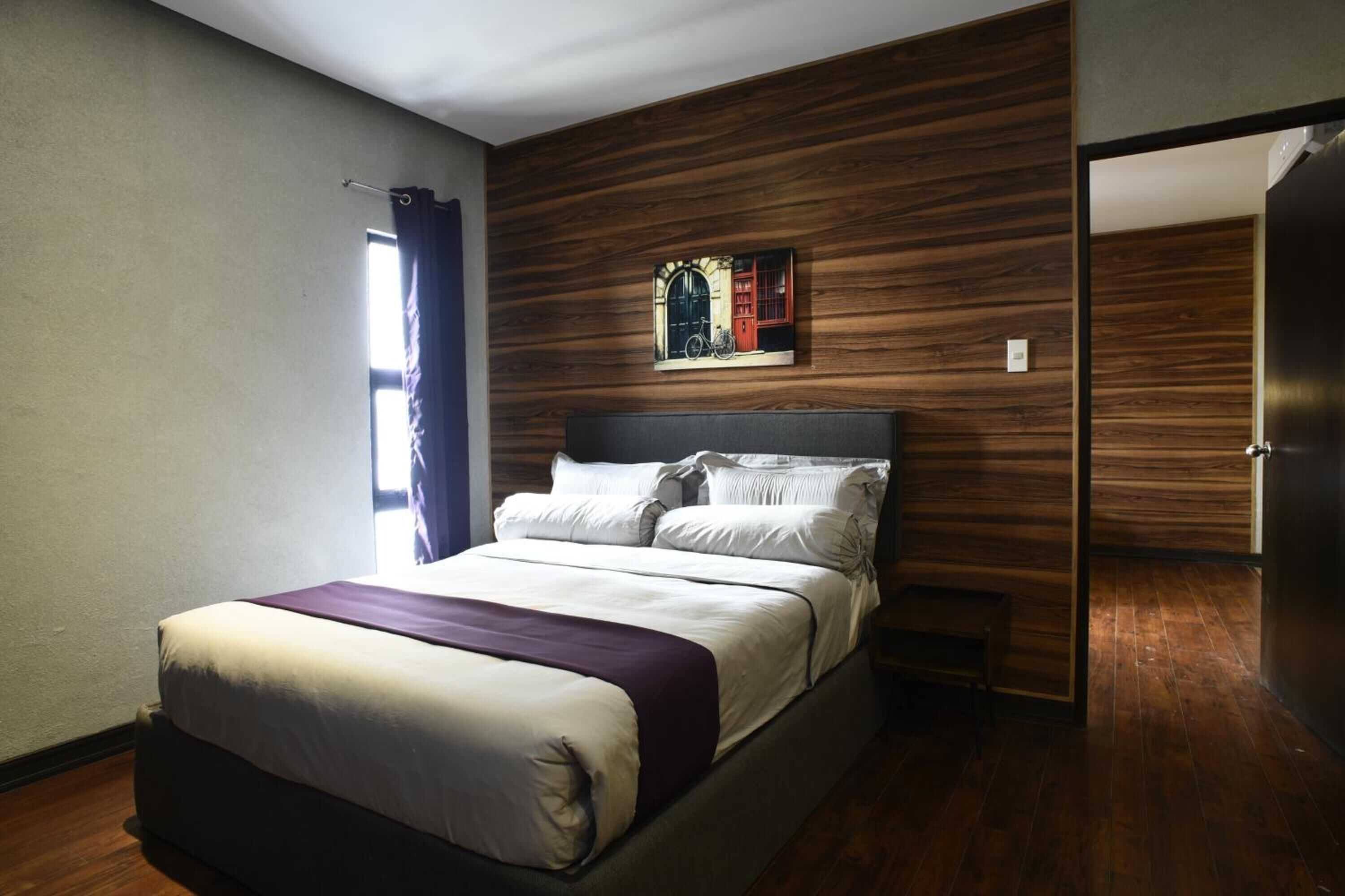 A modern bedroom with a wooden wall panel, a bed with white bedding, and a window with a curtain.