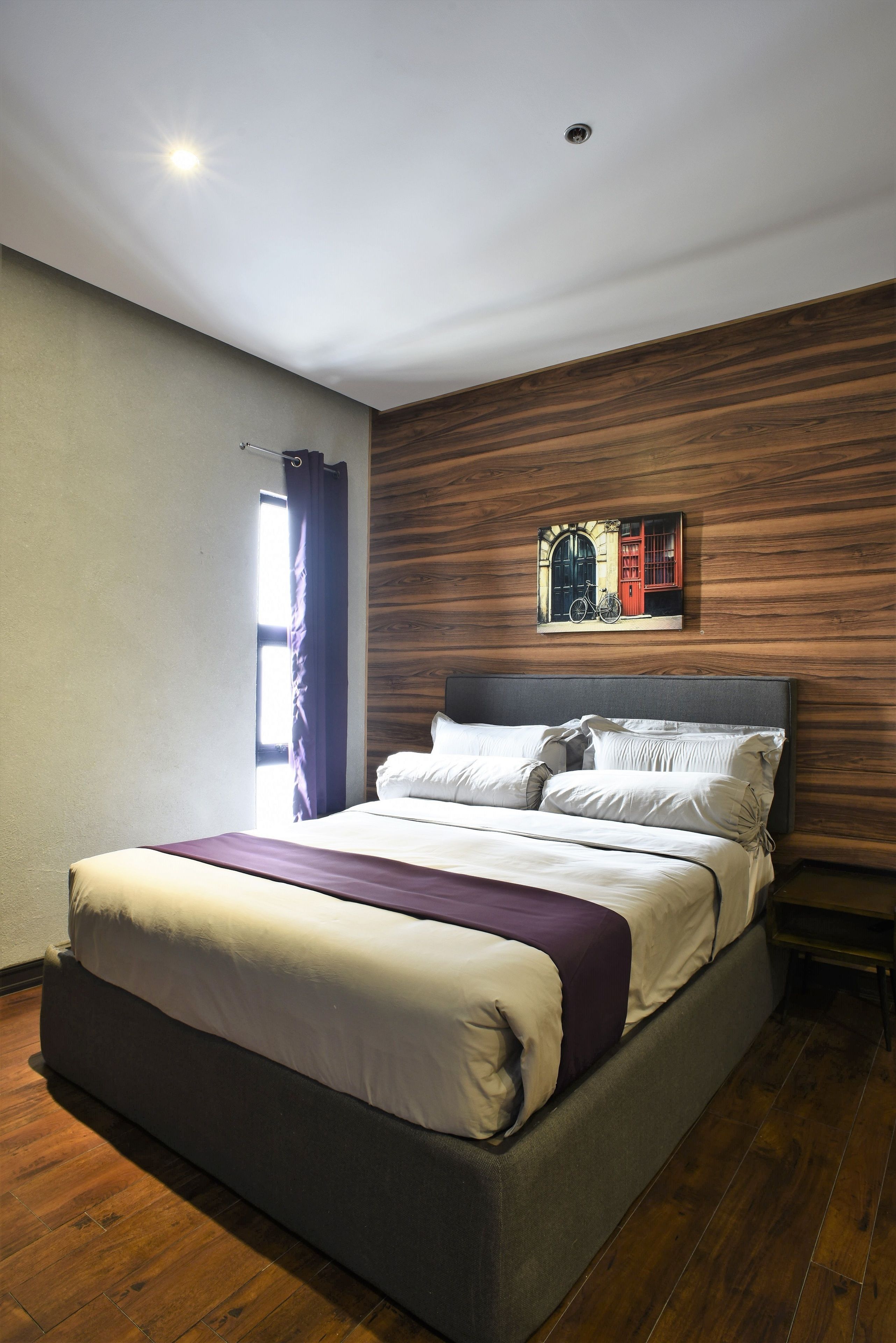 A modern bedroom with a large bed, wooden panel wall, and a window with curtains.