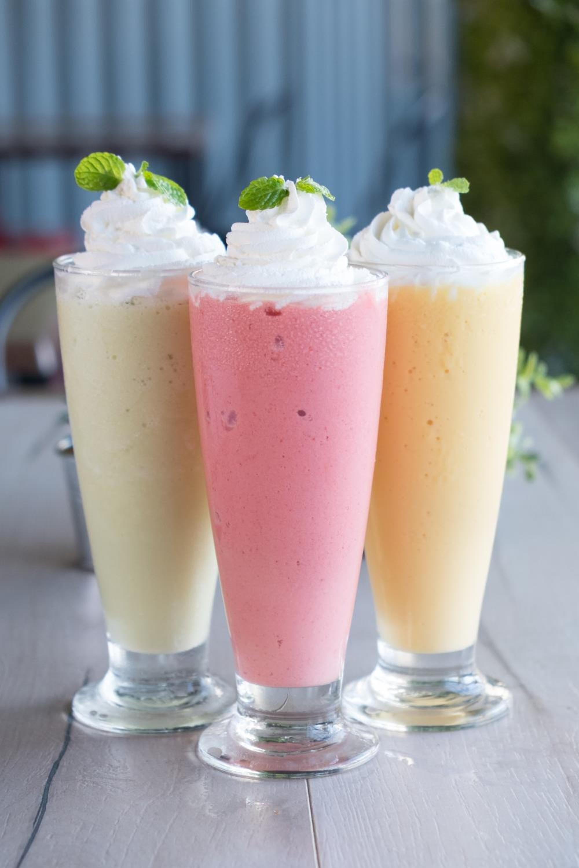 Three tall glasses of layered beverages topped with whipped cream and mint leaves.