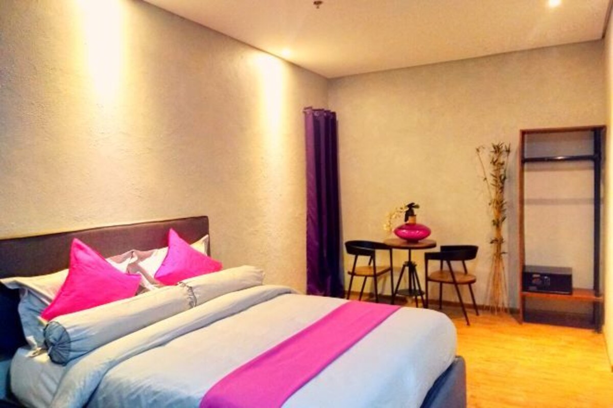 Camera d'albergo con un letto, un piccolo tavolo con sedie, una pianta in vaso e uno specchio.