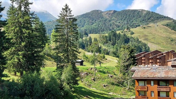 A mountain lodge with a stone facade, multiple balconies, and a view of the surrounding forest and hills. - Family Apartment with Balcony, Ski Access, Upgraded Kitchen & Washer (Valmorel)