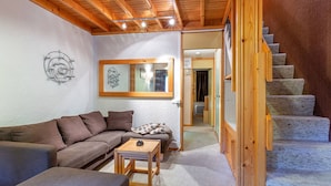 A cozy living room with a wooden ceiling, a sofa, a small table, and a staircase leading to another room. - Family Apartment with Balcony, Ski Access, Upgraded Kitchen & Washer (Valmorel)
