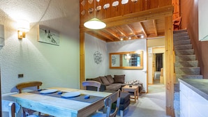 A cozy interior with a wooden dining table, chairs, a sofa, and a staircase leading to another level. - Family Apartment with Balcony, Ski Access, Upgraded Kitchen & Washer (Valmorel)