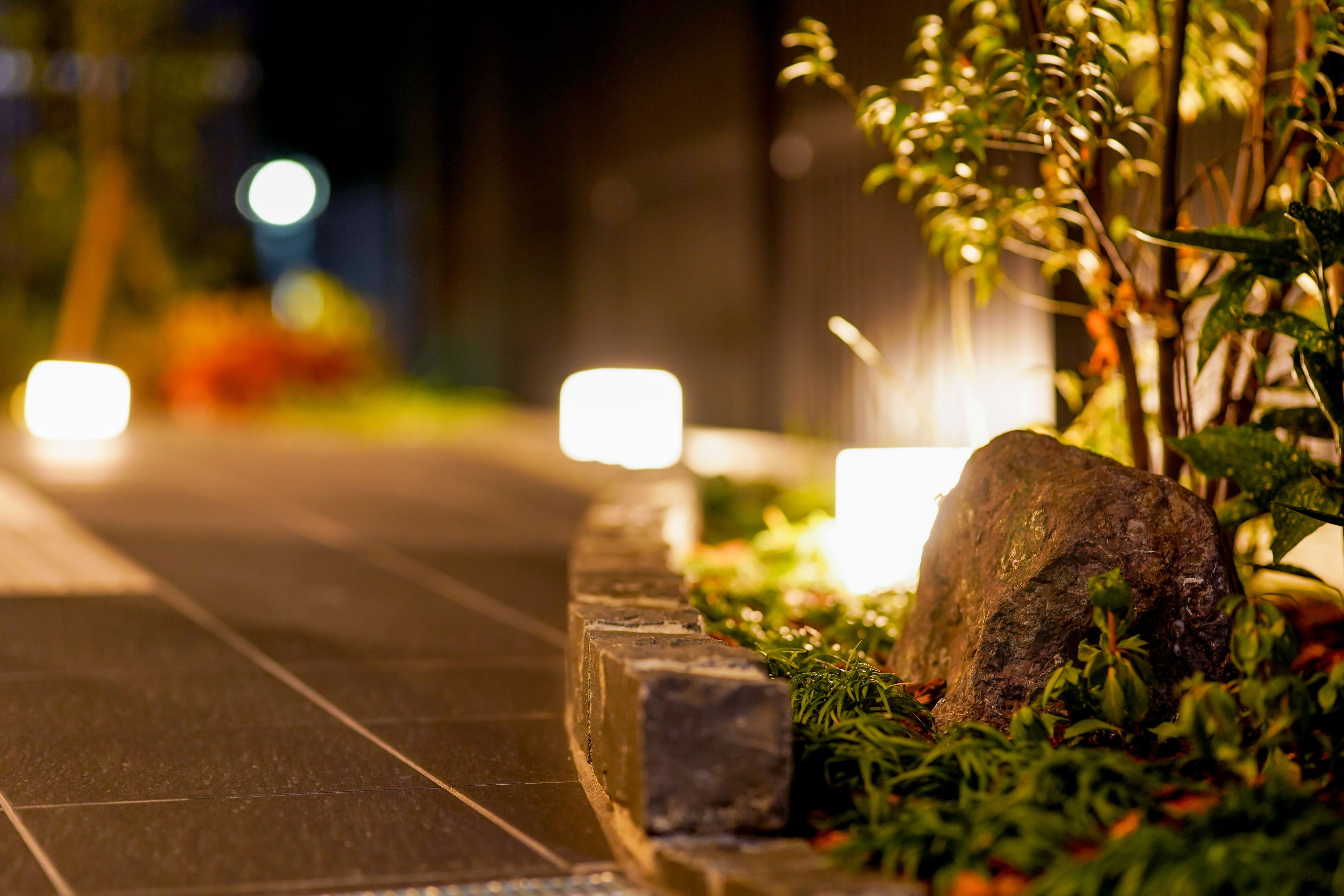 A pathway with stone edging and plants, leading to a large rock.