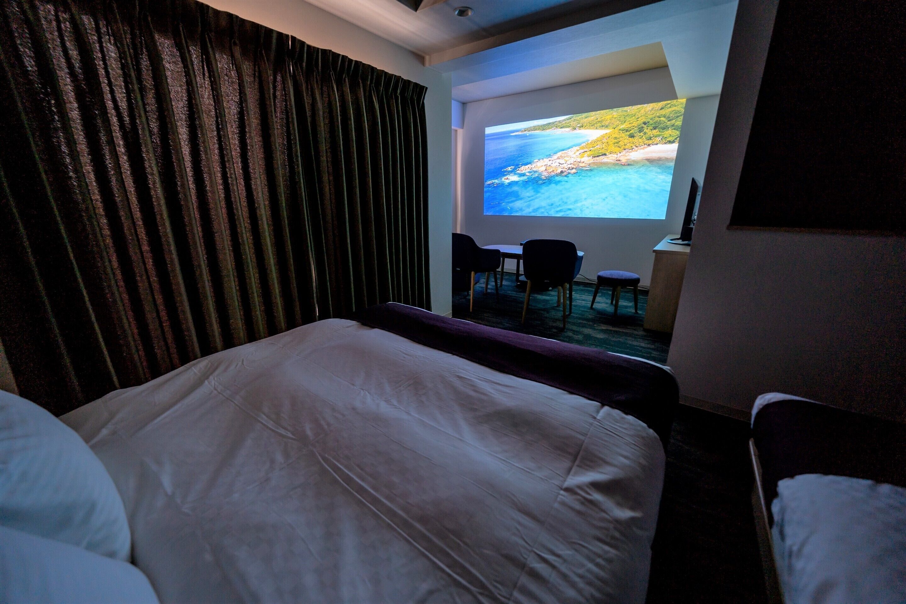 A hotel room with a bed, a desk with a chair, and a large window offering a view of a beach and ocean.