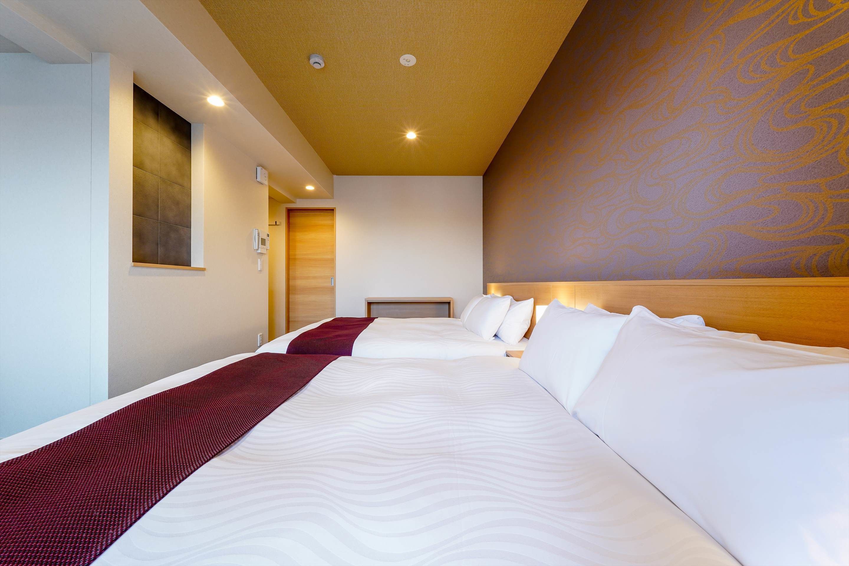 A hotel room with two beds, a red throw blanket, and a wooden headboard.