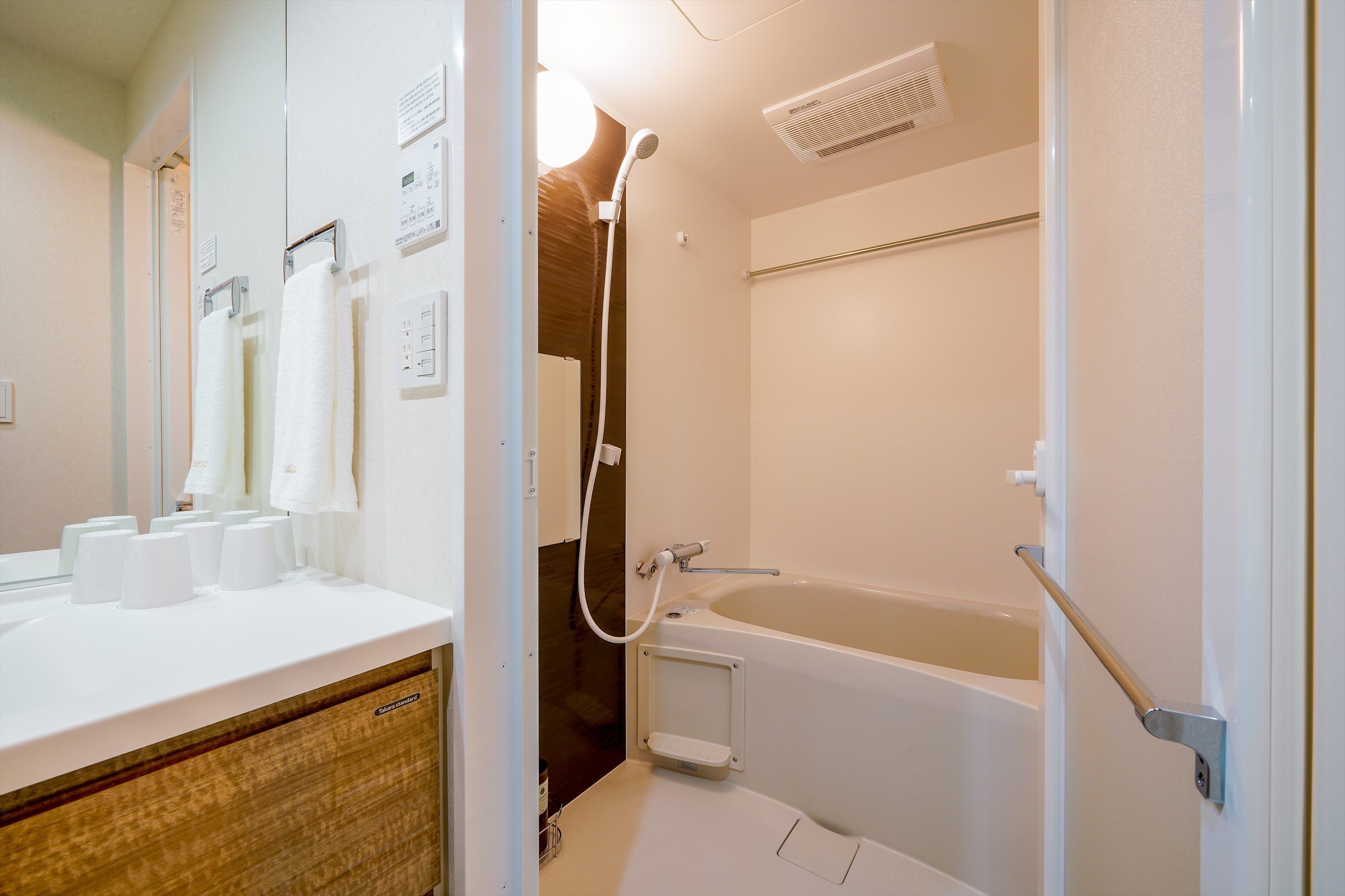 Un bagno con una vasca, una doccia, un lavandino con diversi bicchieri di carta e un portasciugamani con vari asciugamani.