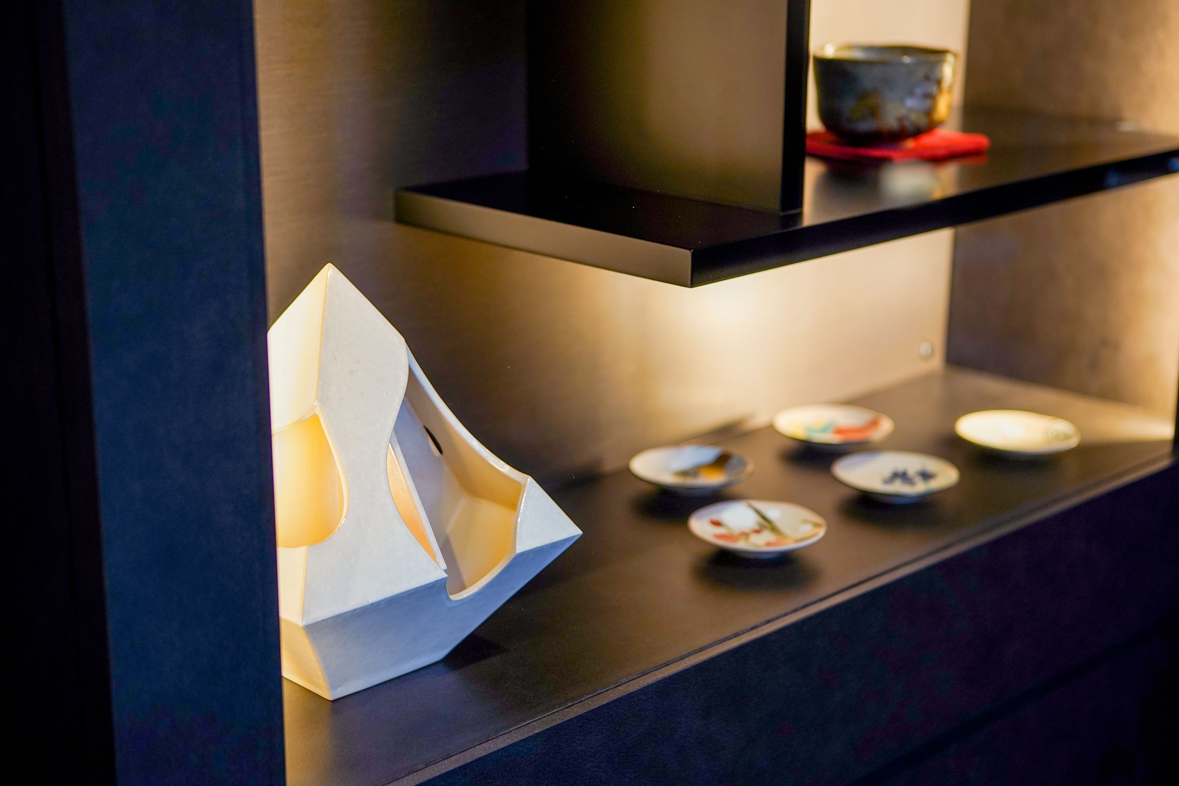 Un intérieur moderne avec une étagère noire élégante où sont exposés de petits plats et un bateau en papier blanc.