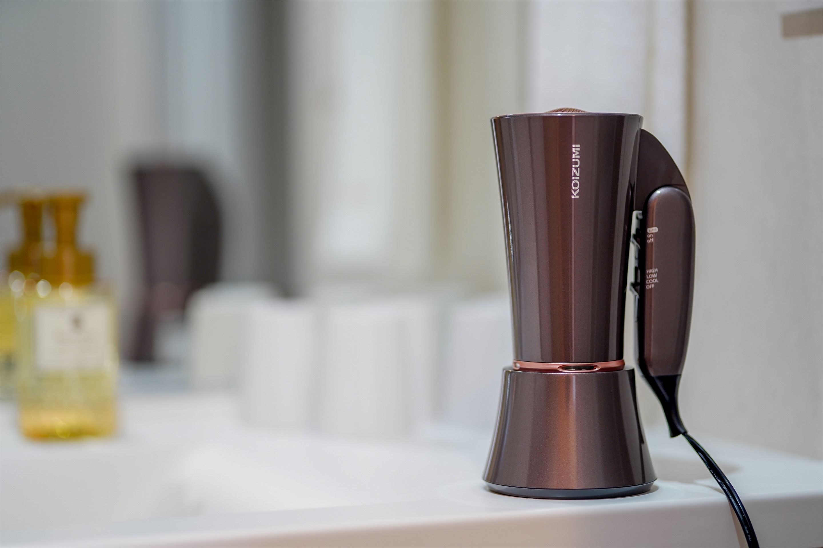 A hairdryer on a white countertop with a bottle of liquid soap in the background.