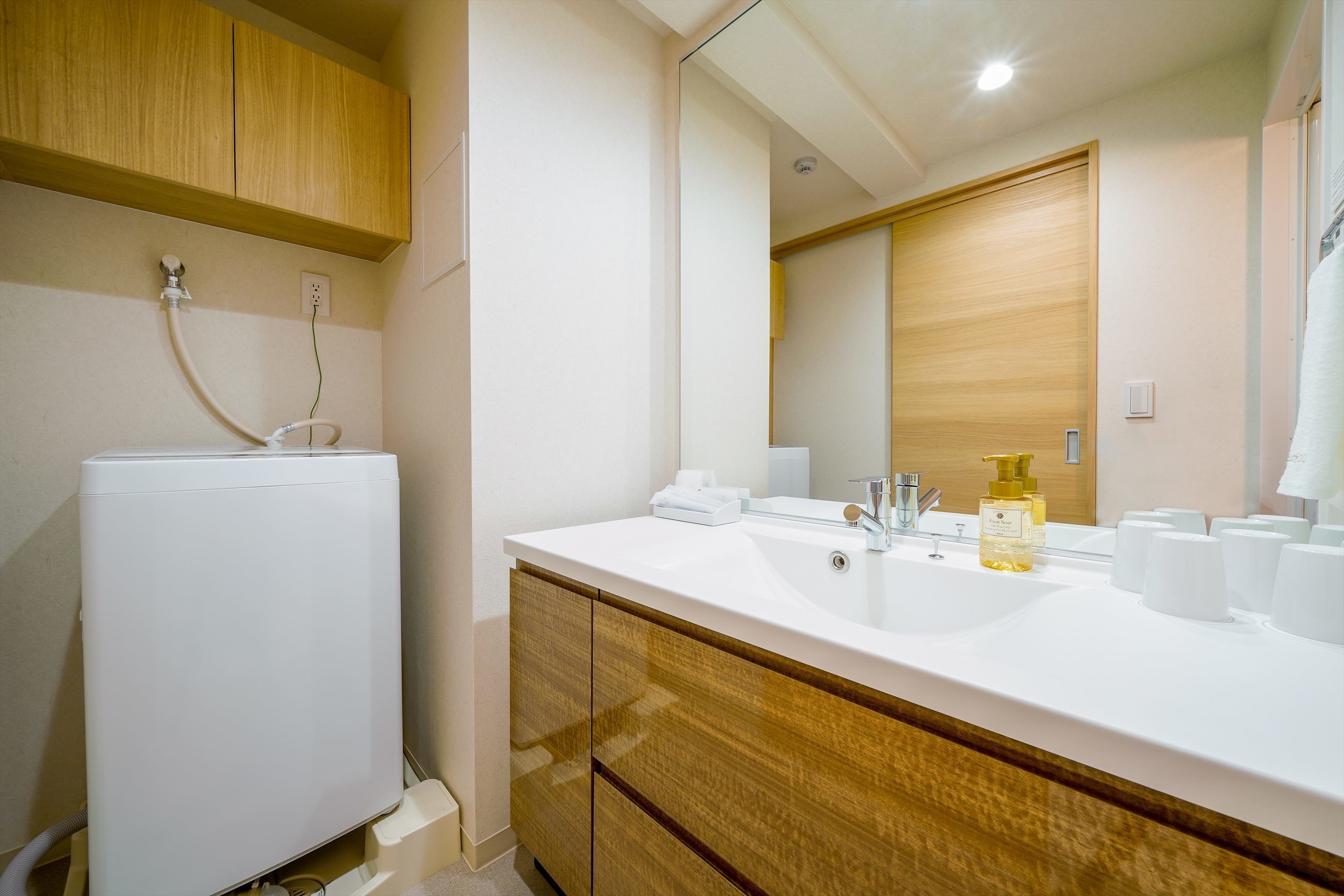 A modern bathroom with a white sink, wooden cabinets, and a large mirror.