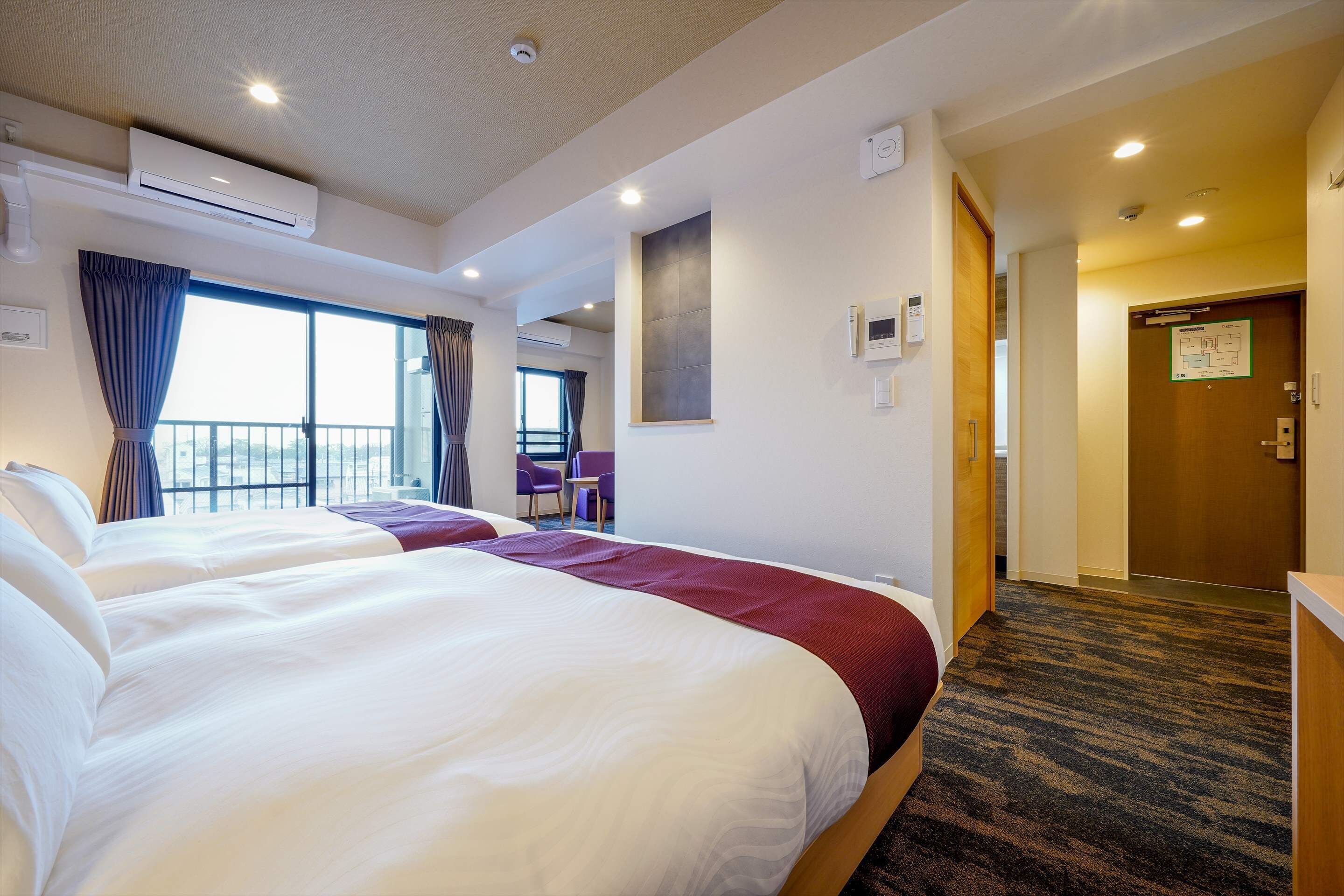 Ein Hotelzimmer mit zwei Betten, einem großen Fenster mit Vorhängen, Blick ins Freie und Teppichboden.