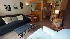 En kompakt opholdsstue med sofa, spisebord og et tekøkken.