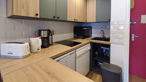 A compact kitchen with wooden cabinets, a microwave, a coffee maker, a toaster, and a dishwasher. - 27m² studio with balcony, pets allowed, near lifts (Valmorel)