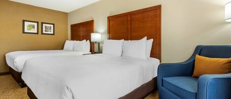 A hotel room with two beds, a blue armchair, and a lamp.