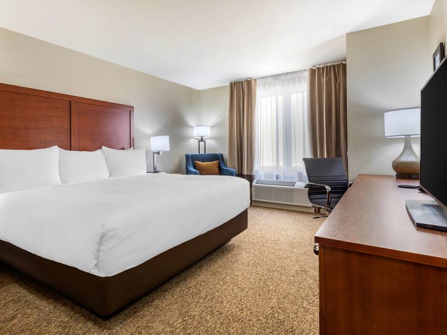 A hotel room with a large bed, a desk with a laptop, a chair, and a television.