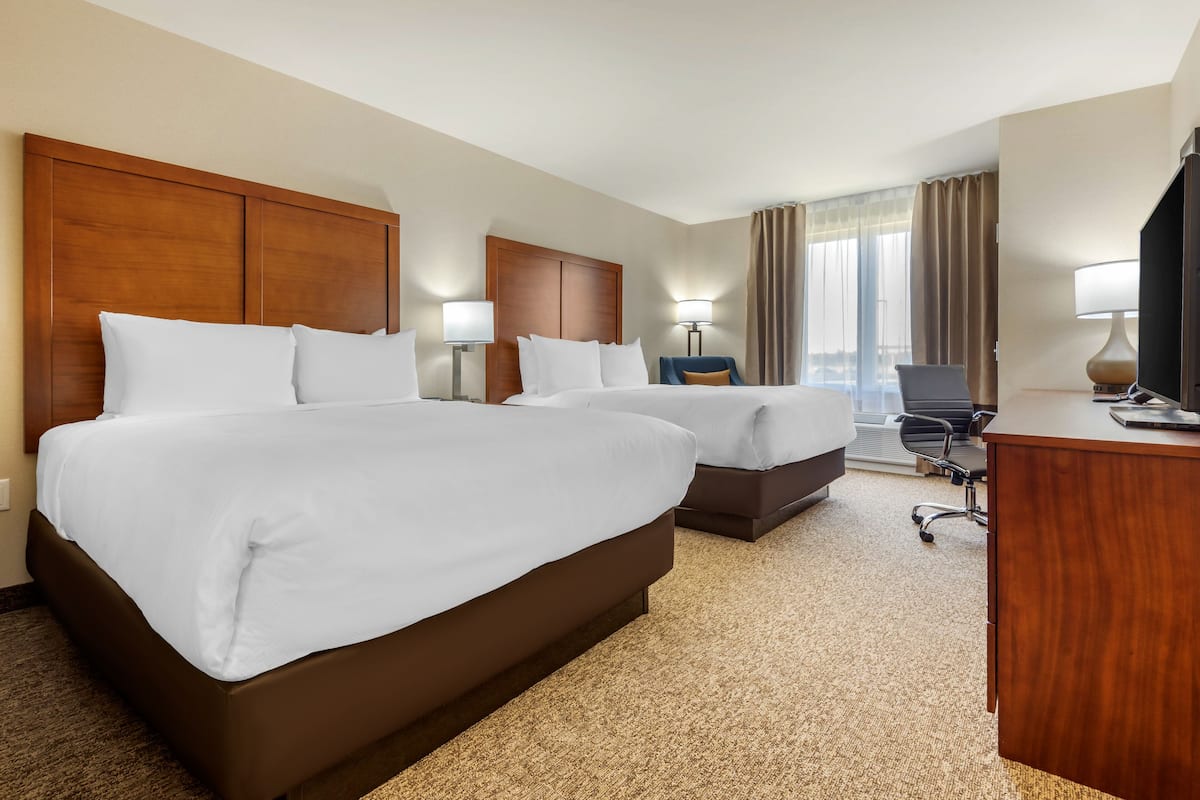 Quarto de hotel com duas camas, uma escrivaninha, uma cadeira e uma televisão.
