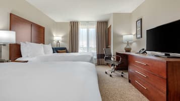A hotel room with two beds, a desk with a TV, a chair, and a lamp.