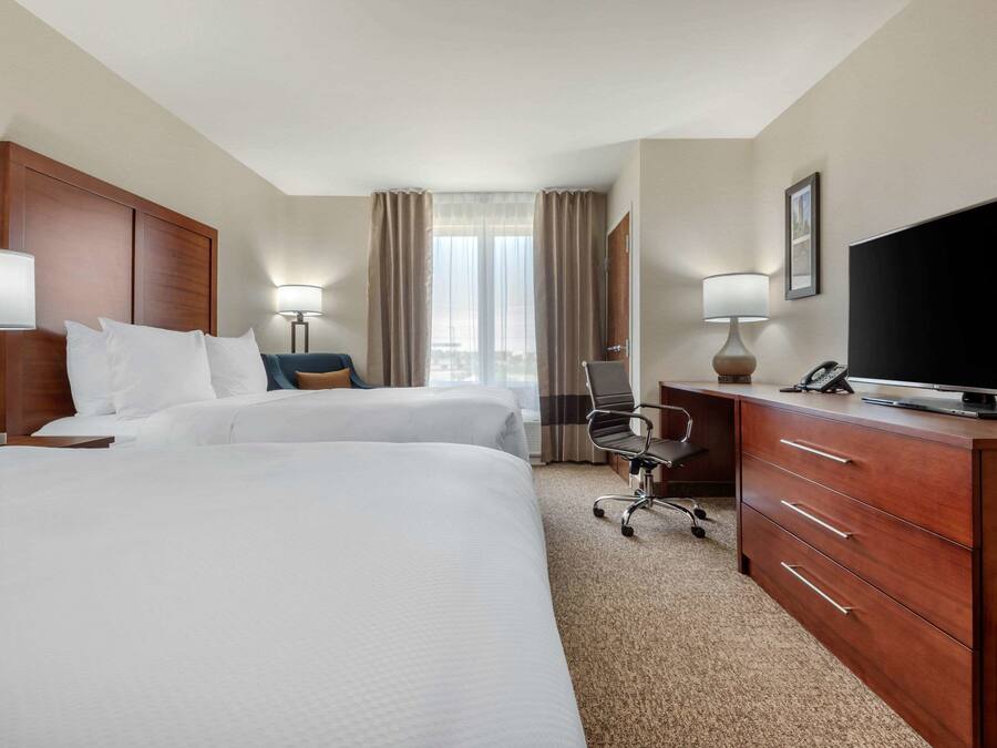 Une chambre d’hôtel avec deux lits, un bureau équipé d’une télévision, une chaise et une lampe.