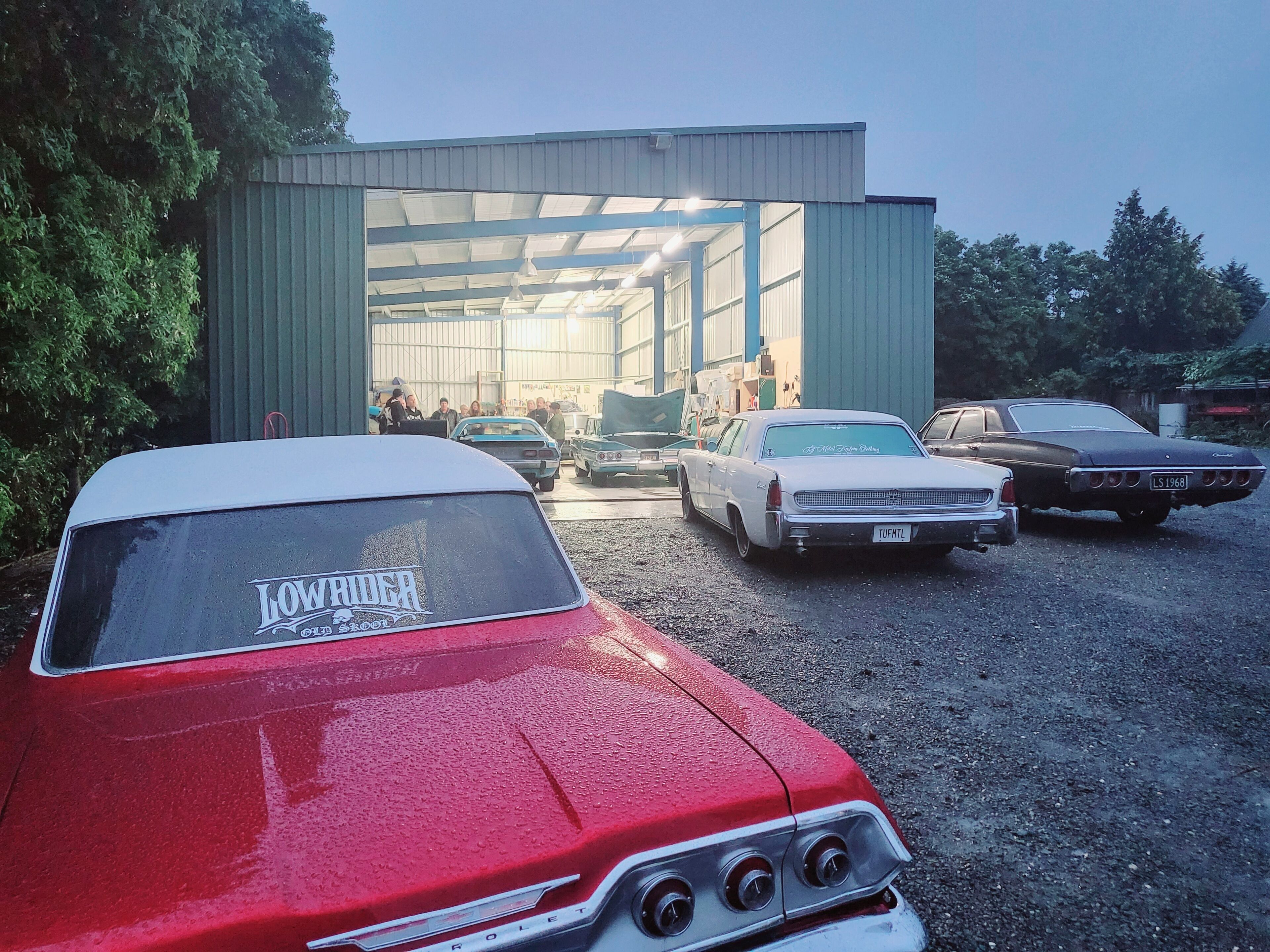 A red vintage car with a visible license plate and a group of people inside a building.