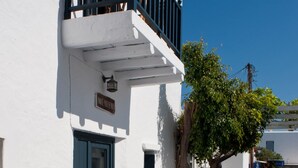 Un edificio blanco con puerta azul y balcón, una calle empedrada de piedra y un cielo azul despejado.