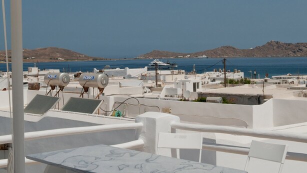 Una terraza en la azotea con mobiliario blanco, una mesa y una sombrilla grande.