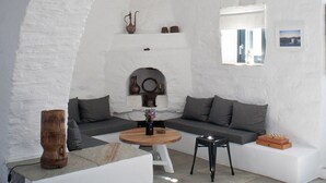 Una habitación con paredes blancas, suelo de piedra, una mesa de madera, un sofá y un taburete pequeño.
