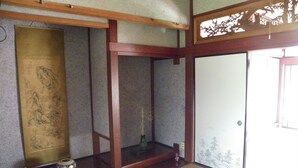 Una habitación japonesa tradicional con suelo de tatami, puerta corredera shoji y un estante de madera con un jarrón y un cuenco pequeño.