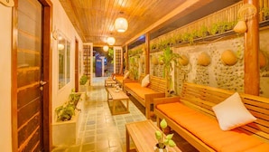 Un pasillo con bancos y mesas de madera, suelo de baldosas y una pared con detalles decorativos y plantas.