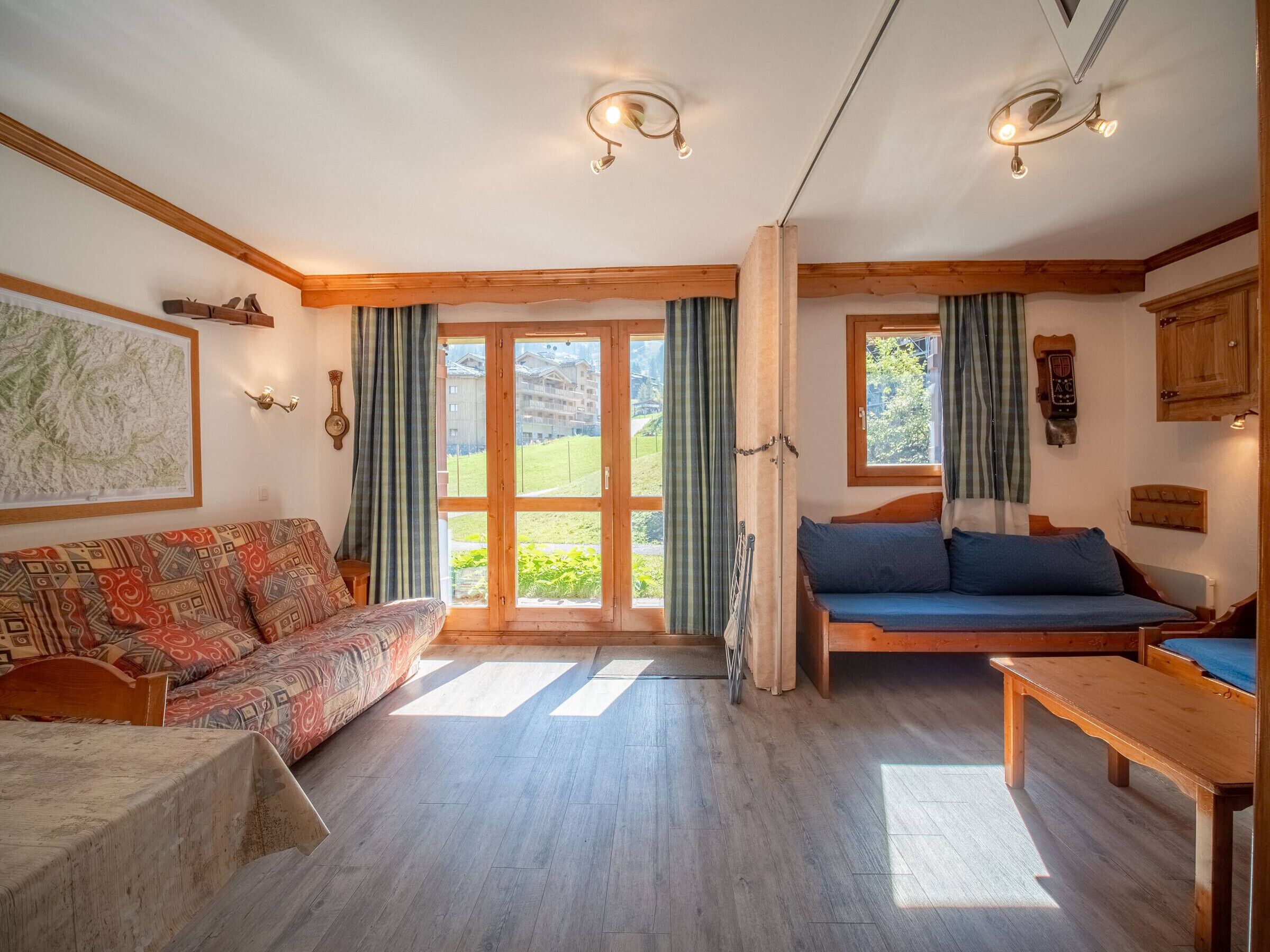 A cozy room with a sofa, a bed, and a wooden bench. There are large windows with curtains, a map on the wall, and a clock.