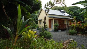 A house with a sloped roof, surrounded by lush greenery and a gravel driveway. - Furnished house in a flower garden for a stay with family and friends (Saint-André)