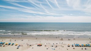 Ein Strand mit Menschen und Sonnenschirmen, bewölkter Himmel und ruhigem Meer.