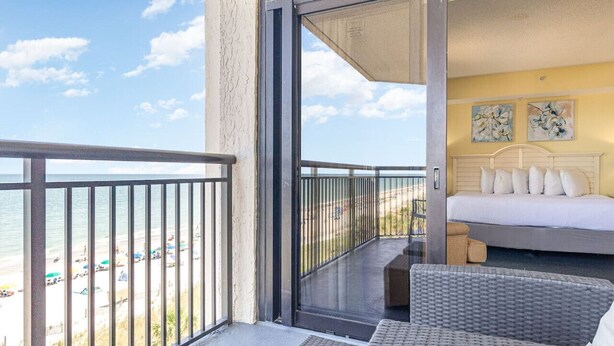 Ein Balkon mit einer Glastür, die zu einem Schlafzimmer mit einem Bett und zwei Bildern an der Wand führt.