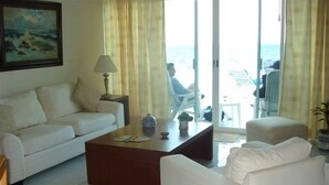 A living room with a white sofa, a wooden coffee table, and a white armchair. There is a painting on the wall and a lamp on a side table. - GREAT PLACE !!!! GREAT PRICE!!!!  WONDERFUL VIEW !!!!   (Puerto Morelos)