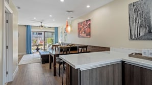 Een moderne keuken met een centraal eiland, houten vloer, hanglampen en een eethoek met stoelen en een tafel.