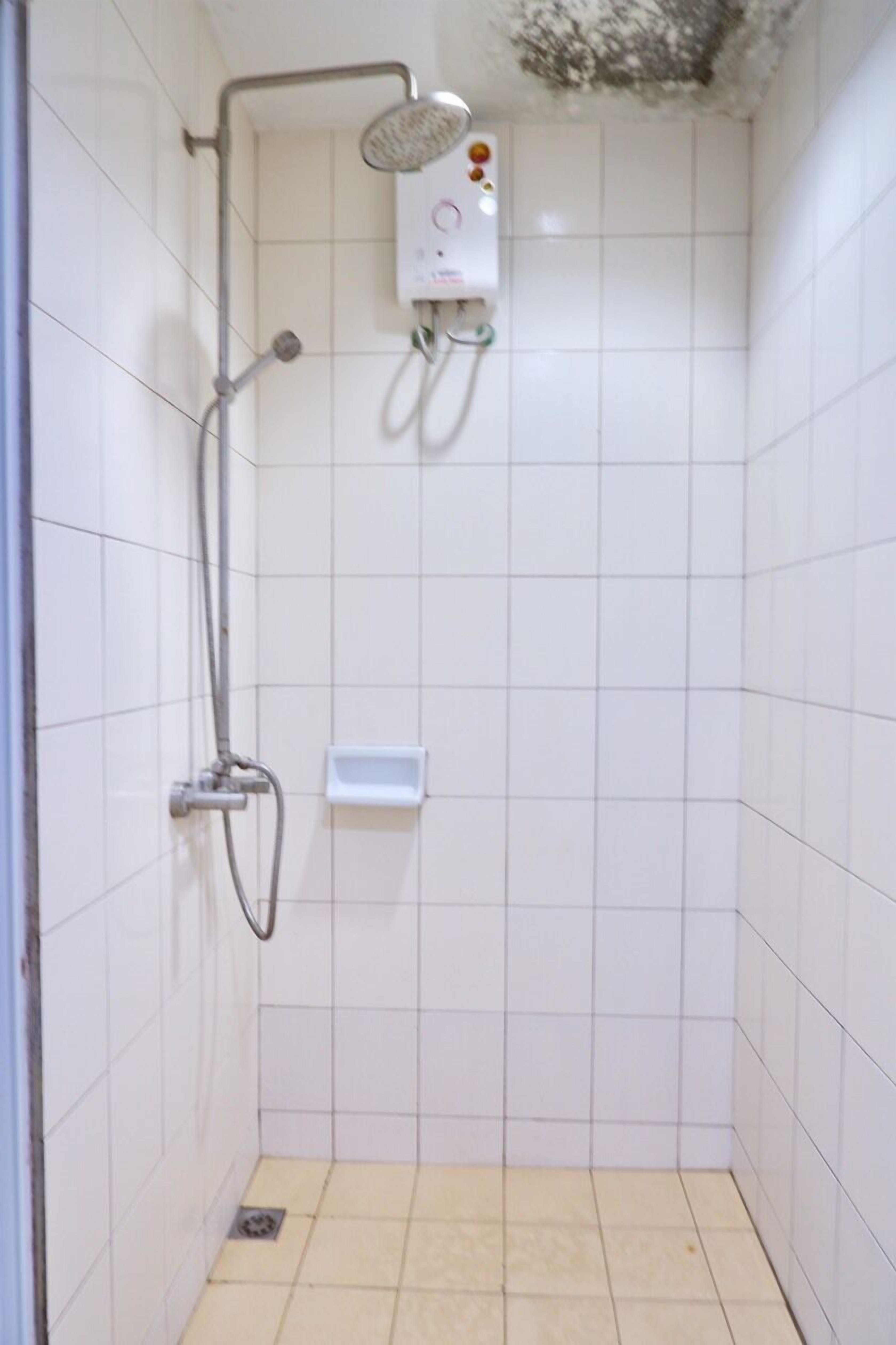 A small, tiled shower room with a handheld showerhead and a wall-mounted control panel.
