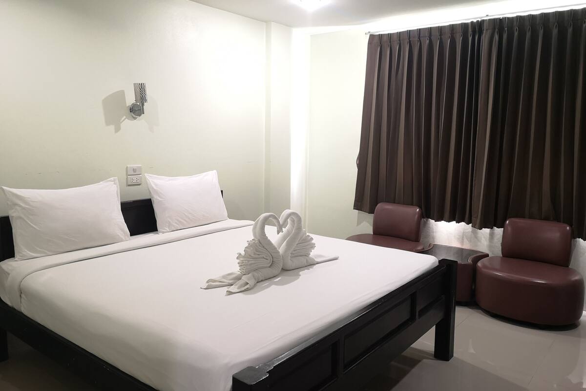 A hotel room with a neatly made bed, a desk with two chairs, and a large window with curtains.
