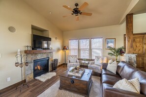 Un salon avec une cheminée, un téléviseur et un ventilateur de plafond.