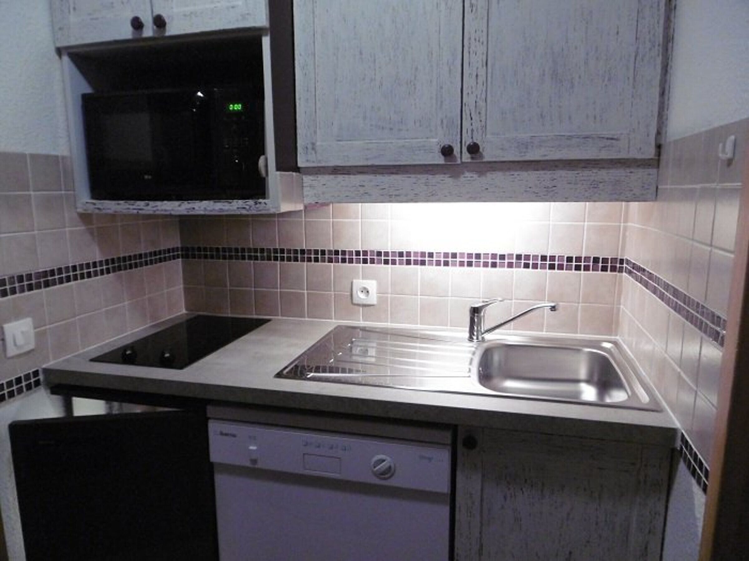 Een kleine keuken met een ingebouwde magnetron, een spoelbak en een vaatwasser.