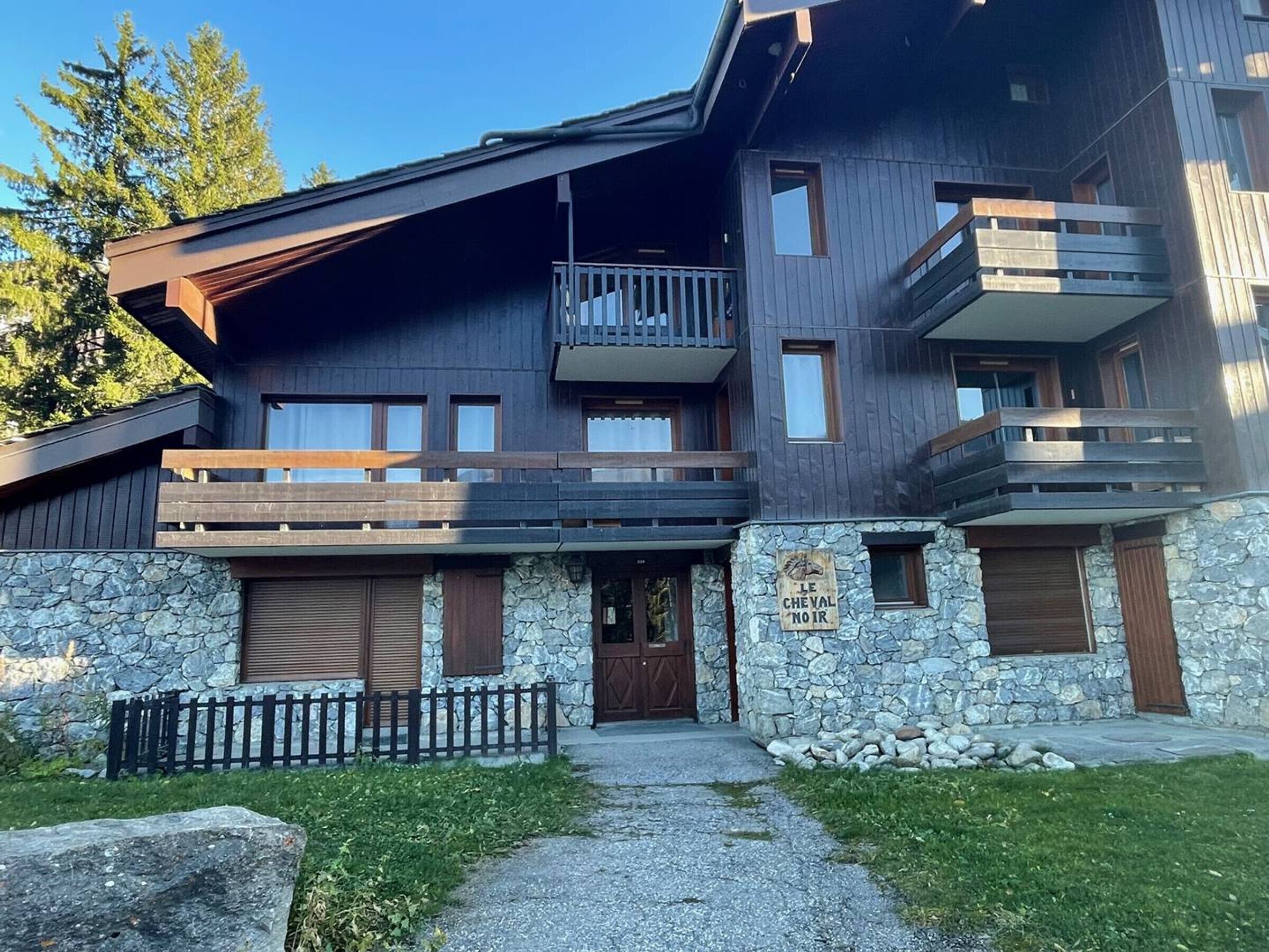 Un immeuble à plusieurs étages, doté d’une façade en pierre, de balcons en bois et d’une enseigne indiquant « LE CHEVAL NOIR ».