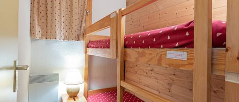 Habitación con literas, suelo de madera, una mesita de noche pequeña con lámpara y una ventana con cortinas.