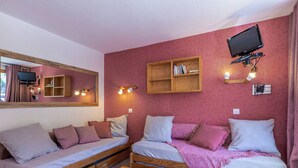 Una habitación acogedora con dos camas de madera, una mesa de madera, un televisor montado en la pared y una estantería.