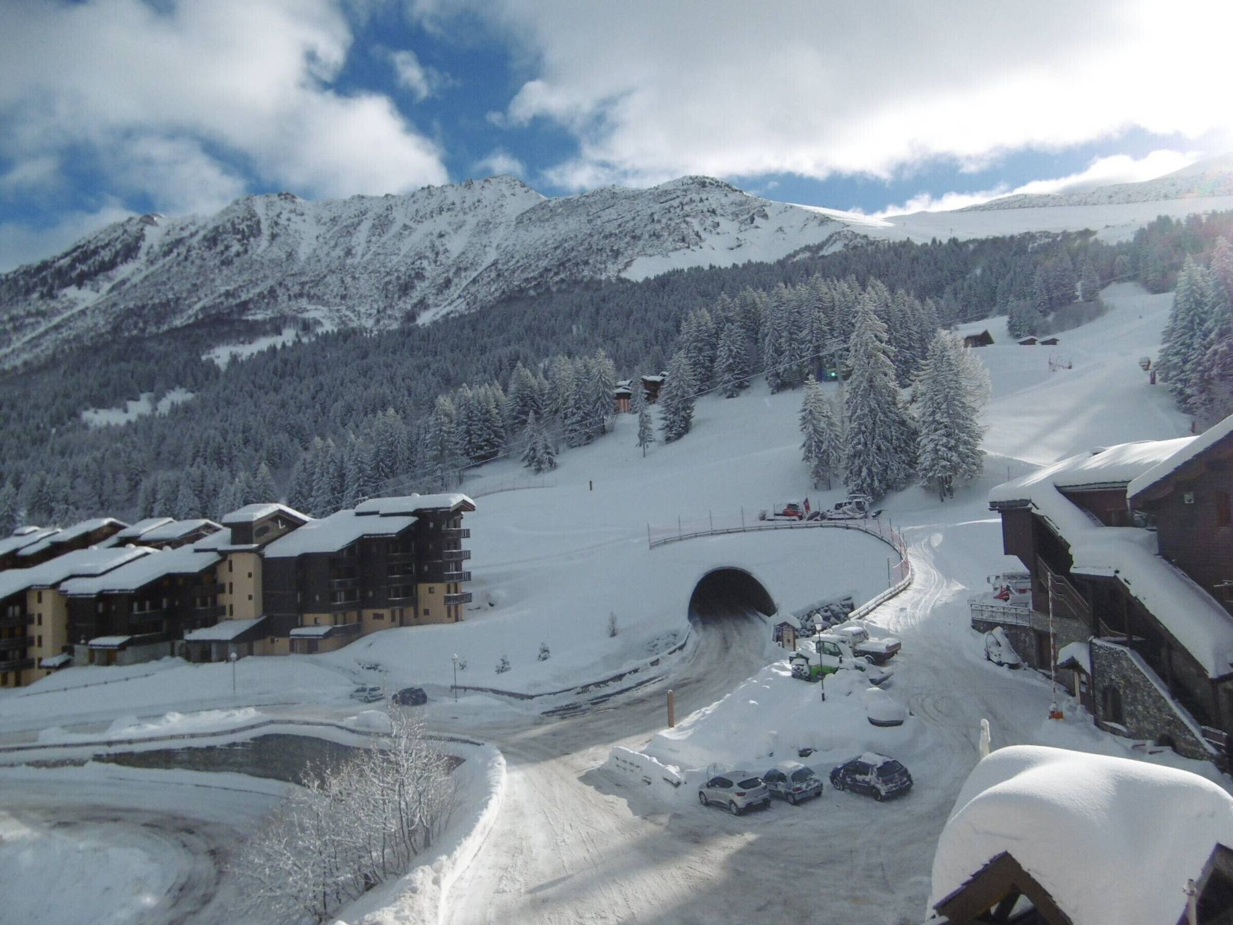 A snow-covered mountain village with buildings, a tunnel, and a ski slope.