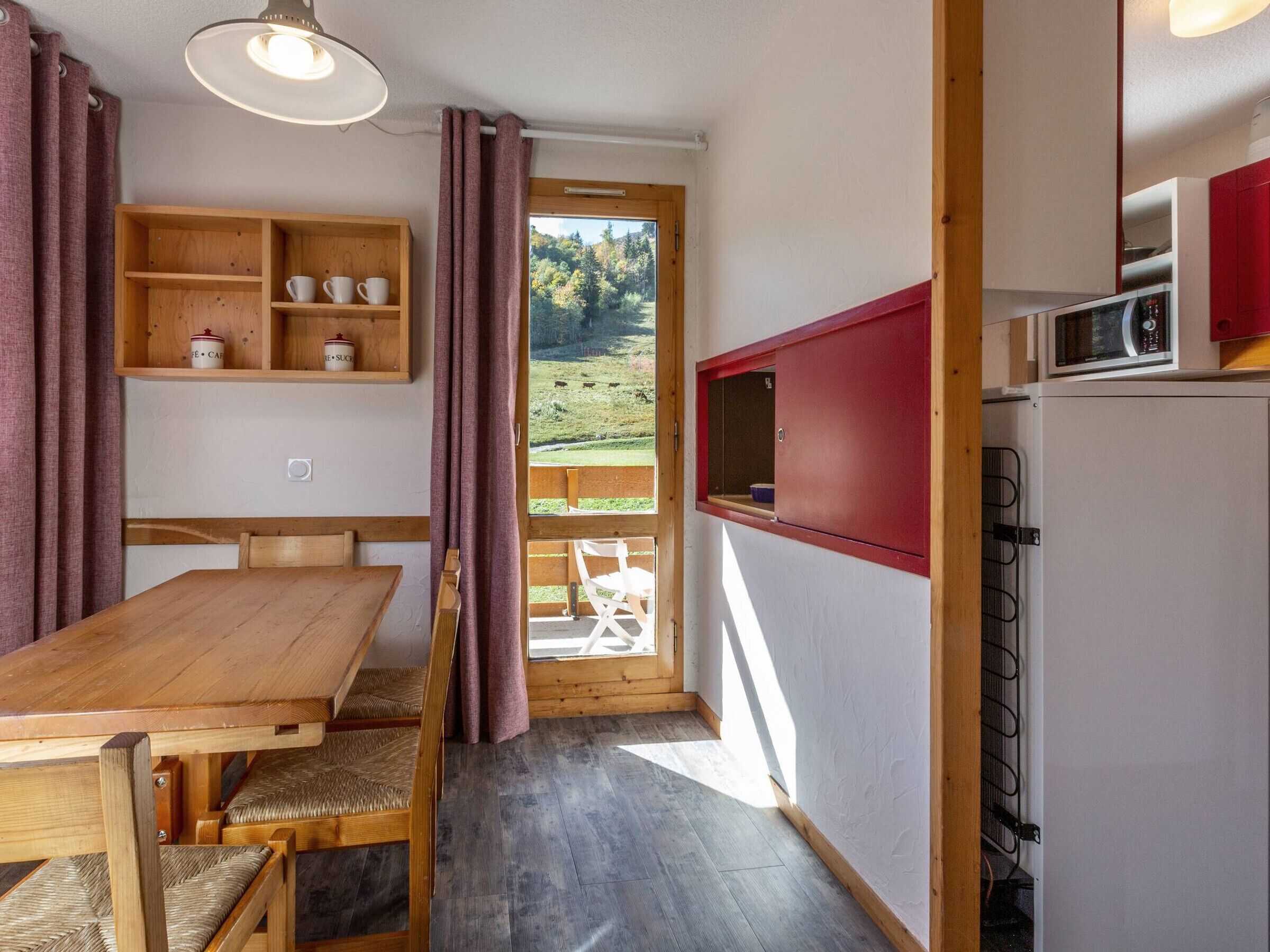Une cuisine compacte avec une table et des chaises en bois, un four à micro-ondes et une vue sur un paysage verdoyant par la fenêtre.