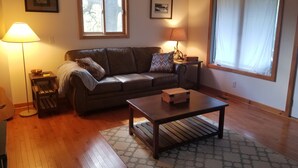 A living room with a brown leather sofa, a wooden coffee table, a lamp, and a window with curtains. - WIFI!! Big Oak Cabin, ozarks, hot tub, rivers! (Tecumseh)