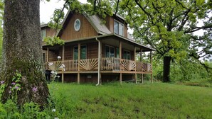 A wooden cabin with a balcony, surrounded by lush greenery and trees. - WIFI!! Big Oak Cabin, ozarks, hot tub, rivers! (Tecumseh)
