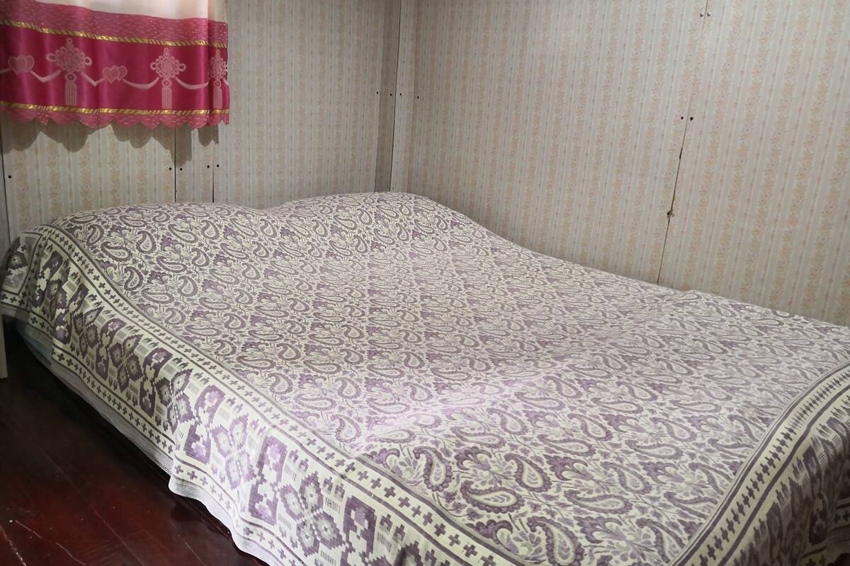 Ein Einzelbett mit einem gemusterten Bettüberwurf in einem Zimmer mit Streifenmuster-Tapete und Holzboden.