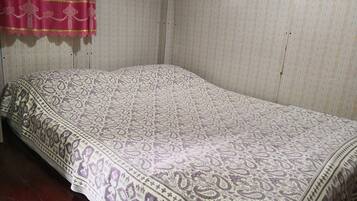 Una cama individual con una colcha estampada en una habitación con papel tapiz a rayas y suelo de madera.