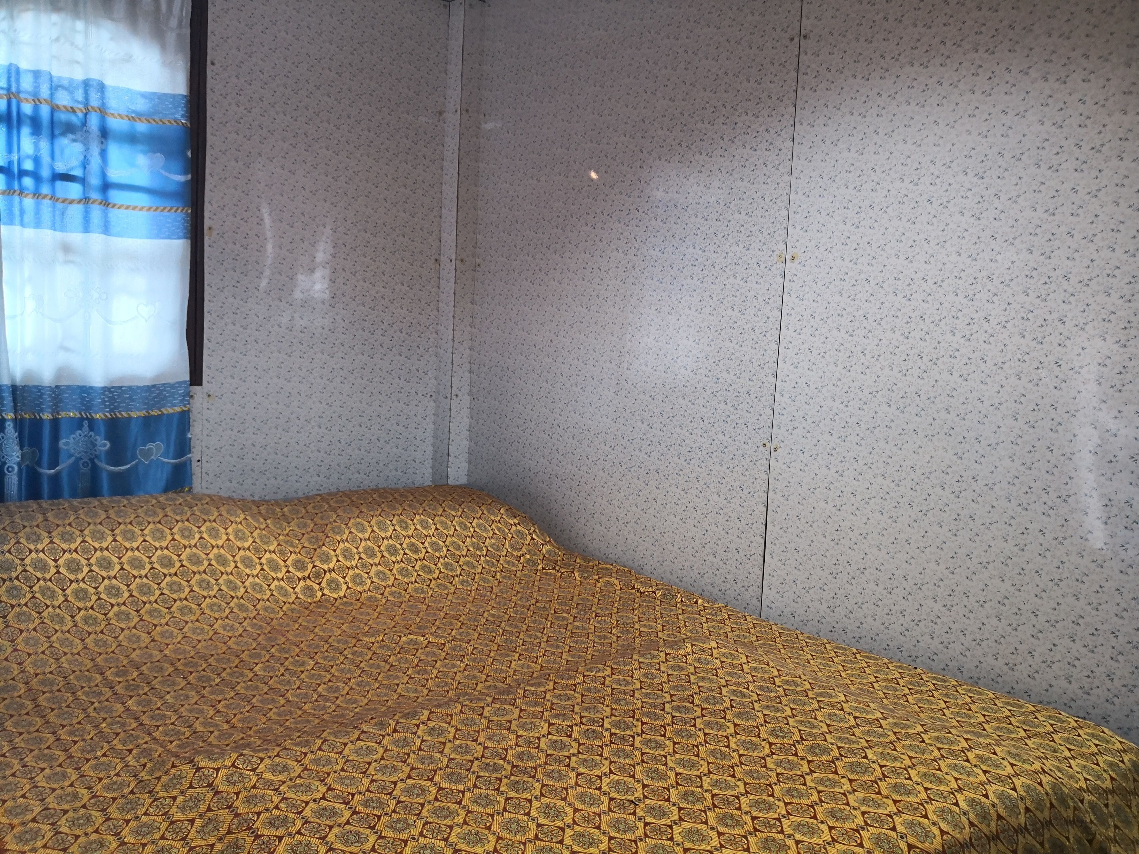Una habitación con una colcha estampada, una cortina con diseño azul y blanco y una pared con textura.